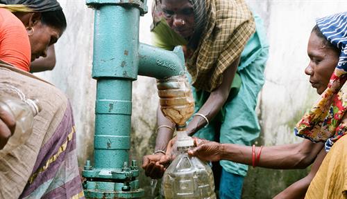 Photo shows women gathered around a shared pump to collect drinking water in Srimongol, Bangladesh.