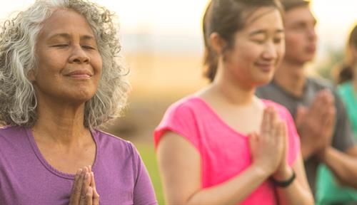 Photo shows a woman smiling while doing meditation with others. Staying cheerful can be protective against stress and some illnesses.