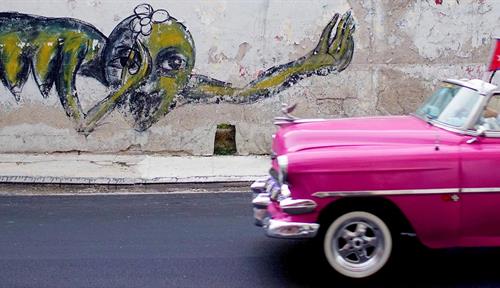 A vintage pink car passes by a graffiti of Cuban Artist Yulier Rodriguez in Havana, Cuba, August 4, 2017.