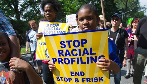 A 2012 photo shows a crowd of marchers, including two young black boys, walking down 5th Avenue in New York City. Their sign reads: “Stop Racial Profiling. End Stop &amp; Frisk.”