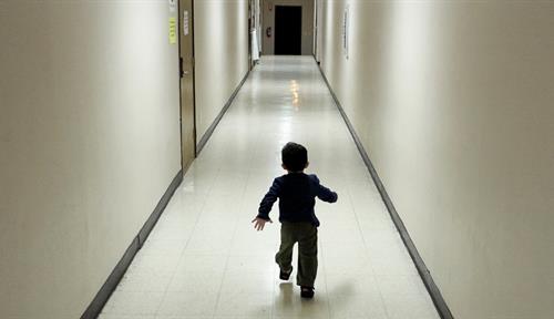 Photo shows a small boy by himself running down the nondescript hall of a shelter.