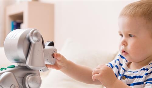 A small boy reaches out to touch a robotic toy dog.