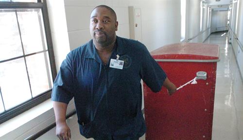 Photo shows a Black hospital worker pulling a trash container down a hallway.