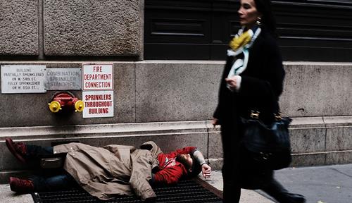 A wealthy woman walks past a homeless man on the street.